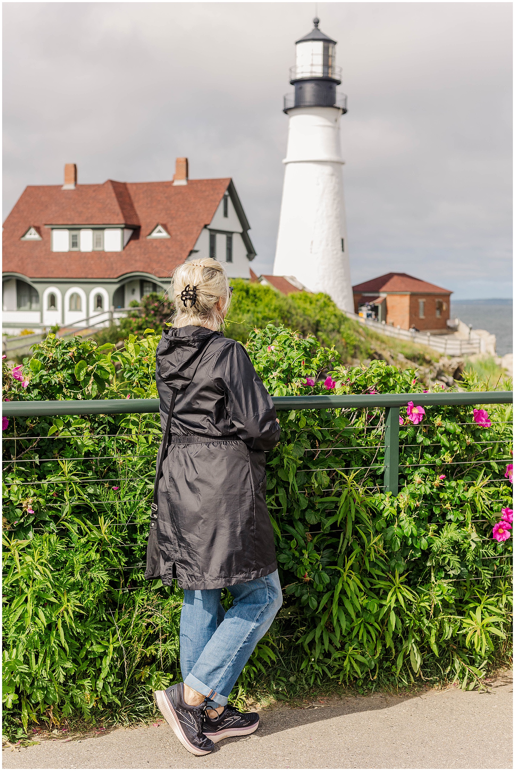 woman standing in a rain coat looking at a lighthouse for things to do in maine