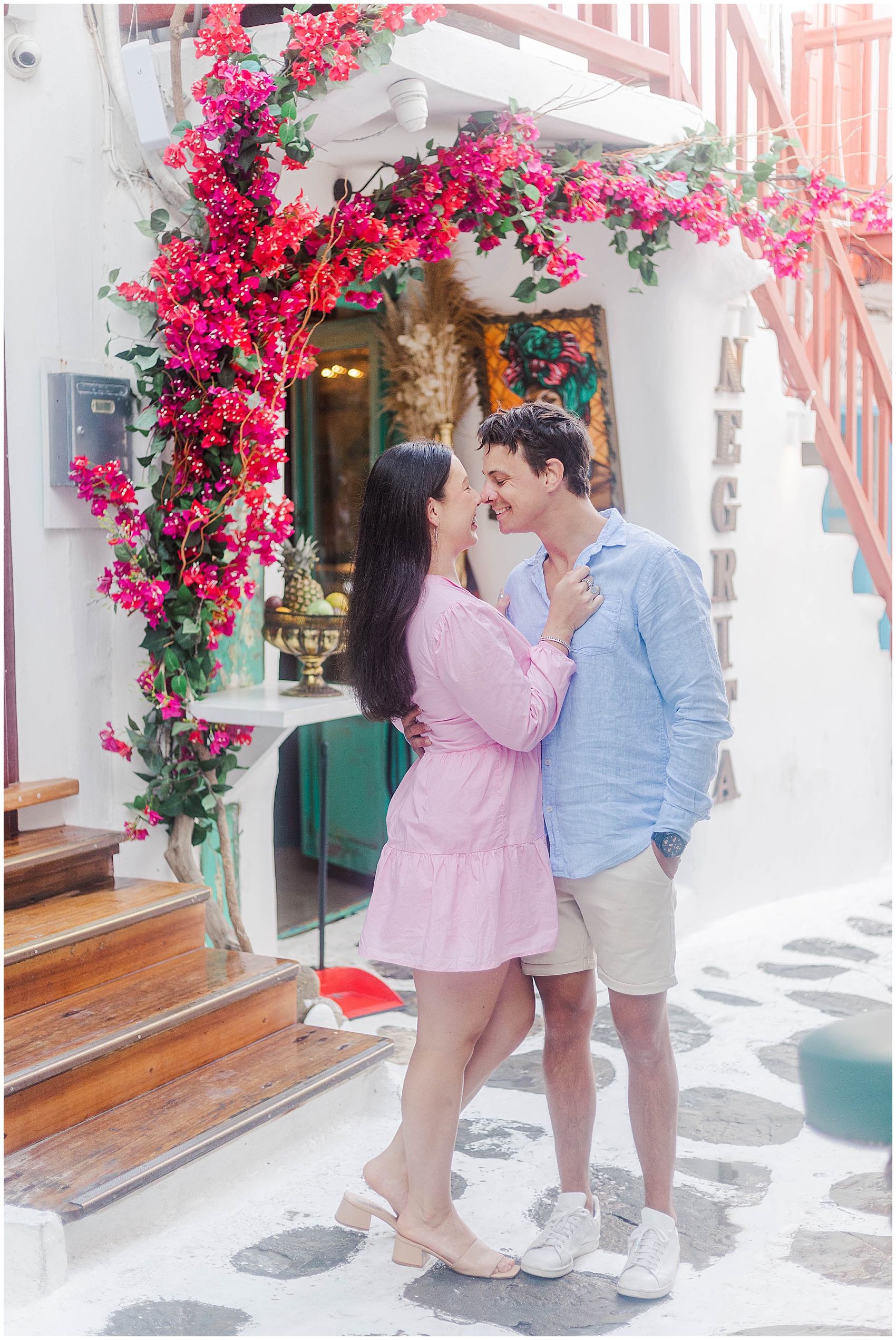 couple in pink and blue standing under pink flowers during greece photoshoot