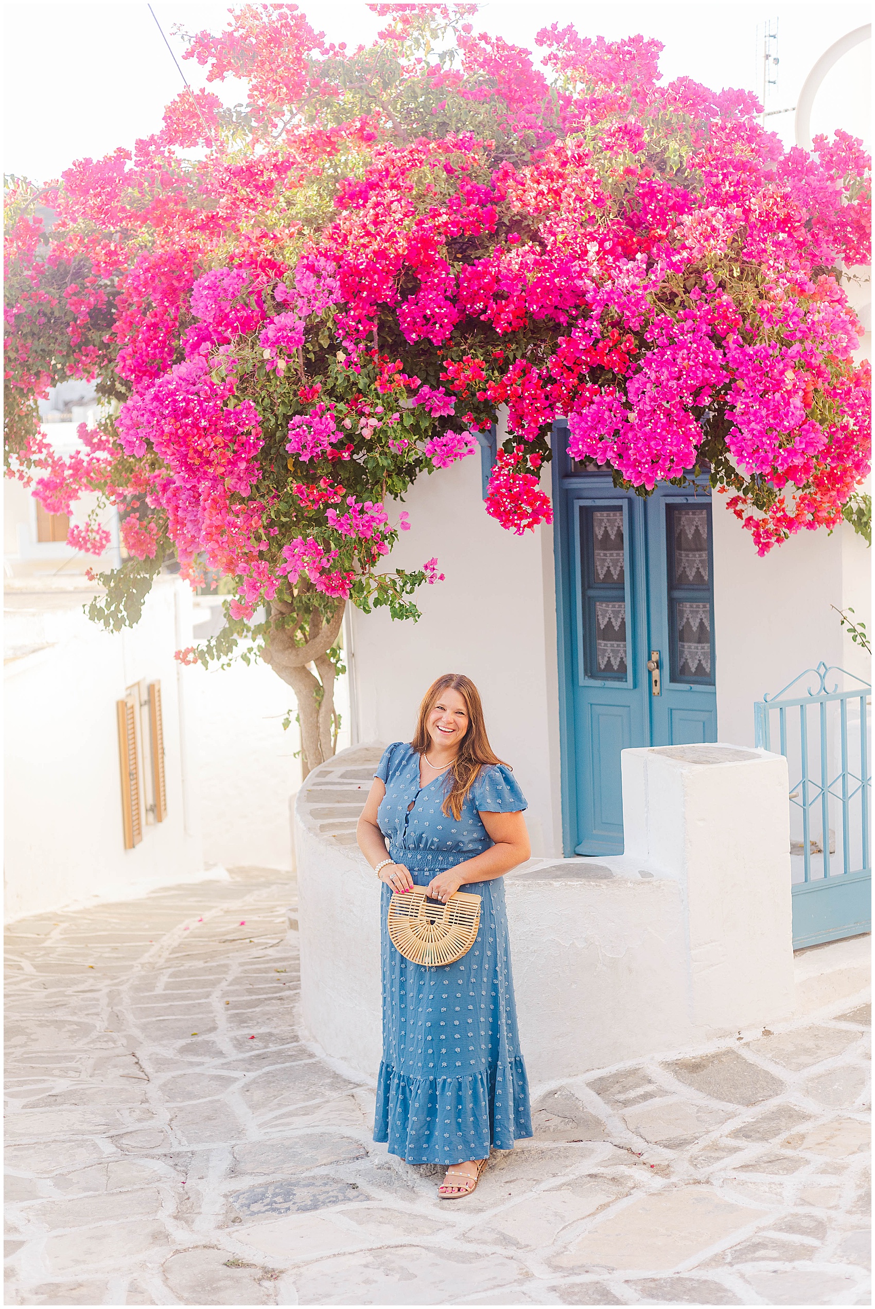 woman in blue dress standing under pink flowers greece photoshoot