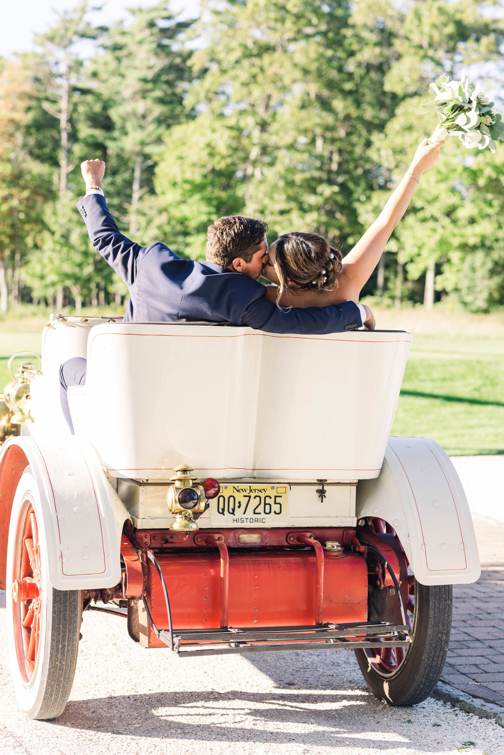 bride and groom driving away in an old car with their arms in the air at their Bay Club Mattapoisett wedding